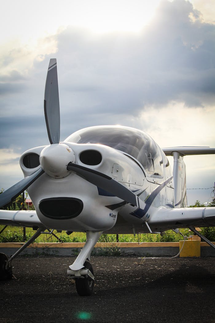 gallery-6 A compact single-engine aircraft stands ready on the runway beneath cloudy skies, perfect for aviation enthusiasts.