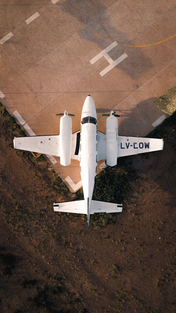 about-img Aerial top view of white airplane with propellers on edge of paved airfield in light